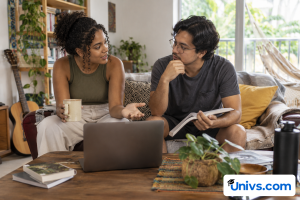 Two students discussing a university residence or private rental decision in a comfortable modest shared living room, no identifiable property